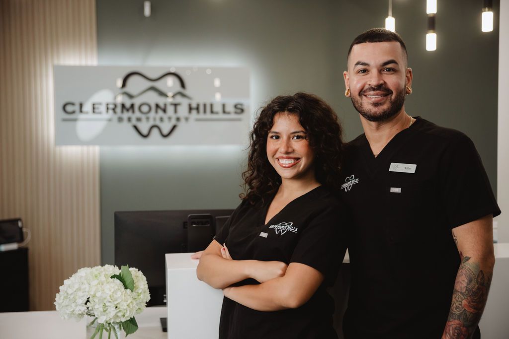 Two people smiling, wearing black scrubs, in a dental office reception area. 