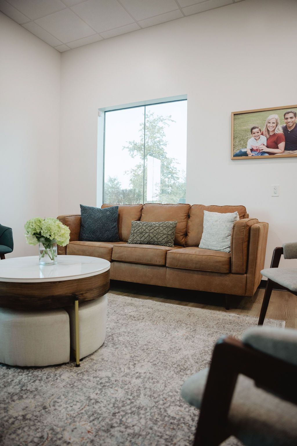 Cozy waiting room with brown sofa, round coffee table, and framed family photo. Neutral colors.
