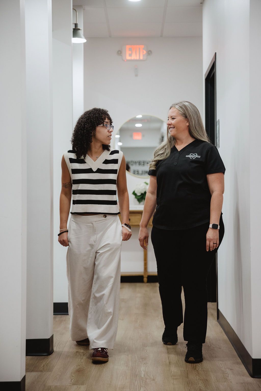 Woman in scrubs walks alongside a patient in a hallway, smiling and talking.