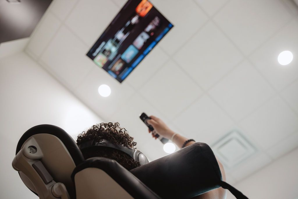 Person reclined in chair, watching TV mounted on ceiling, holding remote control.