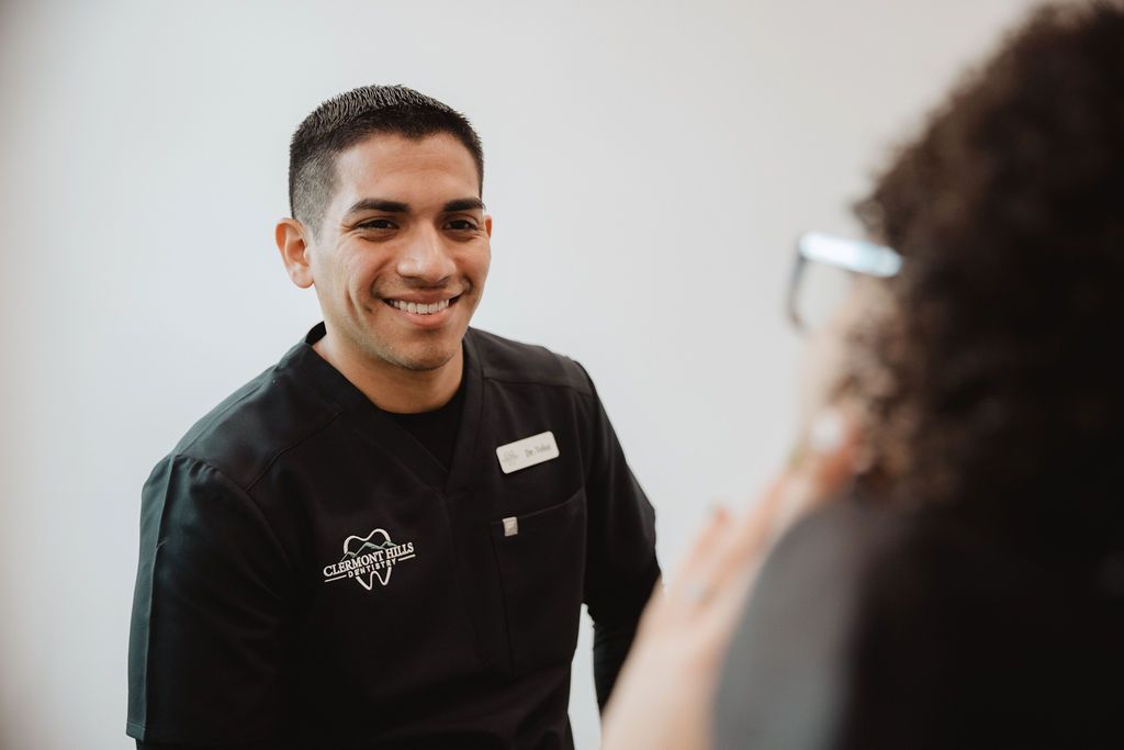Man in black scrubs smiles, looking at a person out of frame. White wall background.