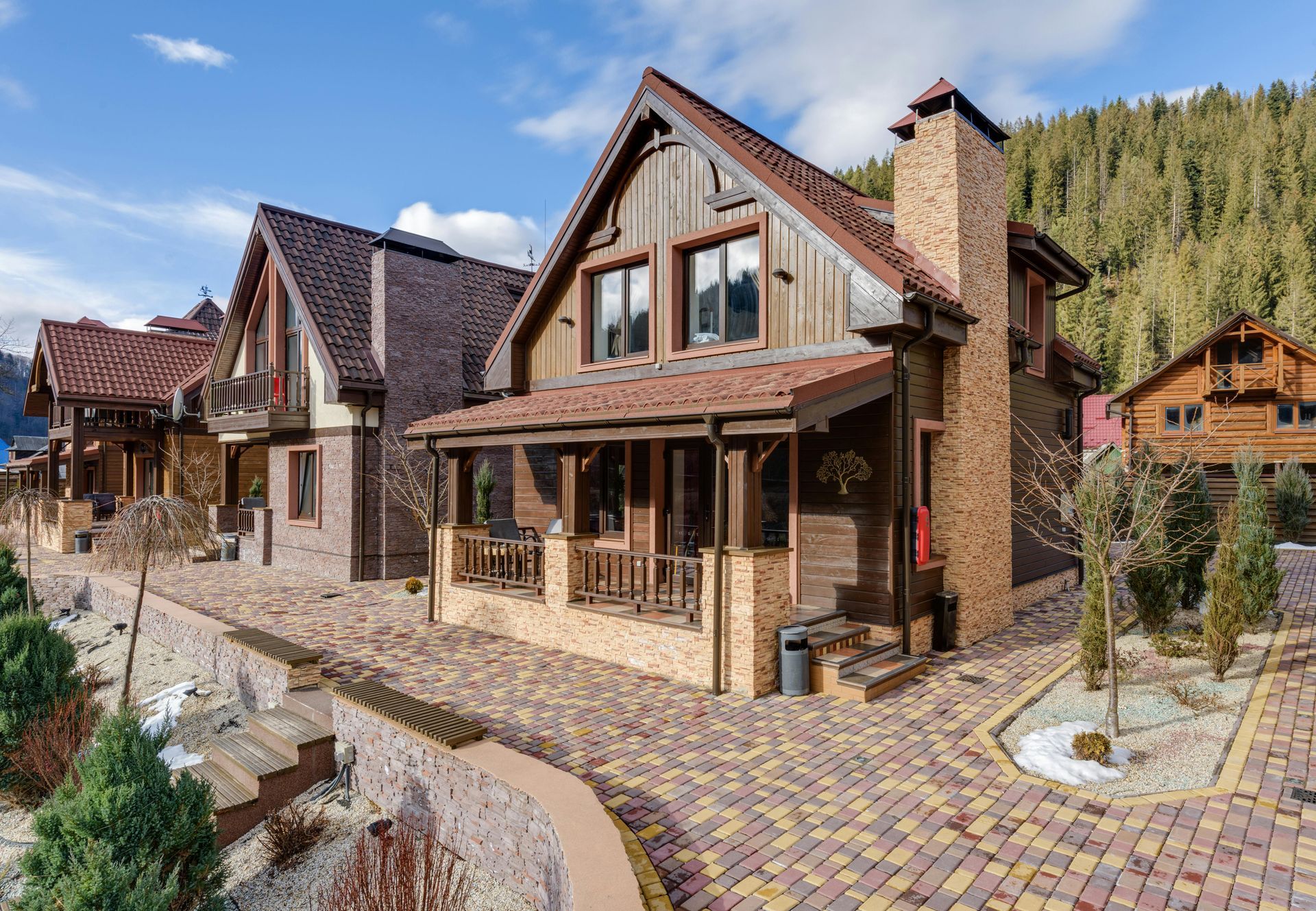 Brown wood and brick cabins with gabled roofs, a cobblestone pathway, and a forest backdrop.