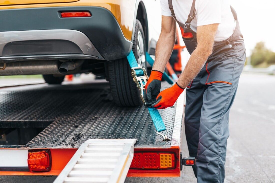 Tow truck technician fastening straps to car wheels