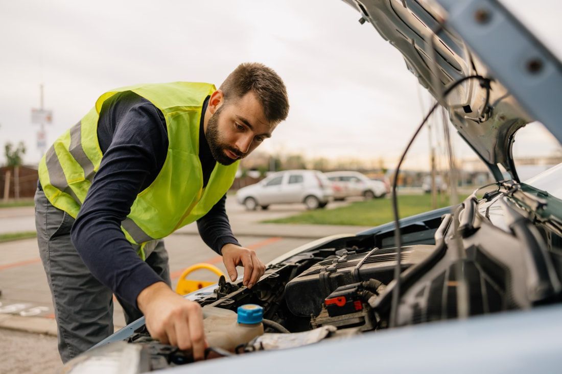 Man with reflective vest looking under the hood of a car