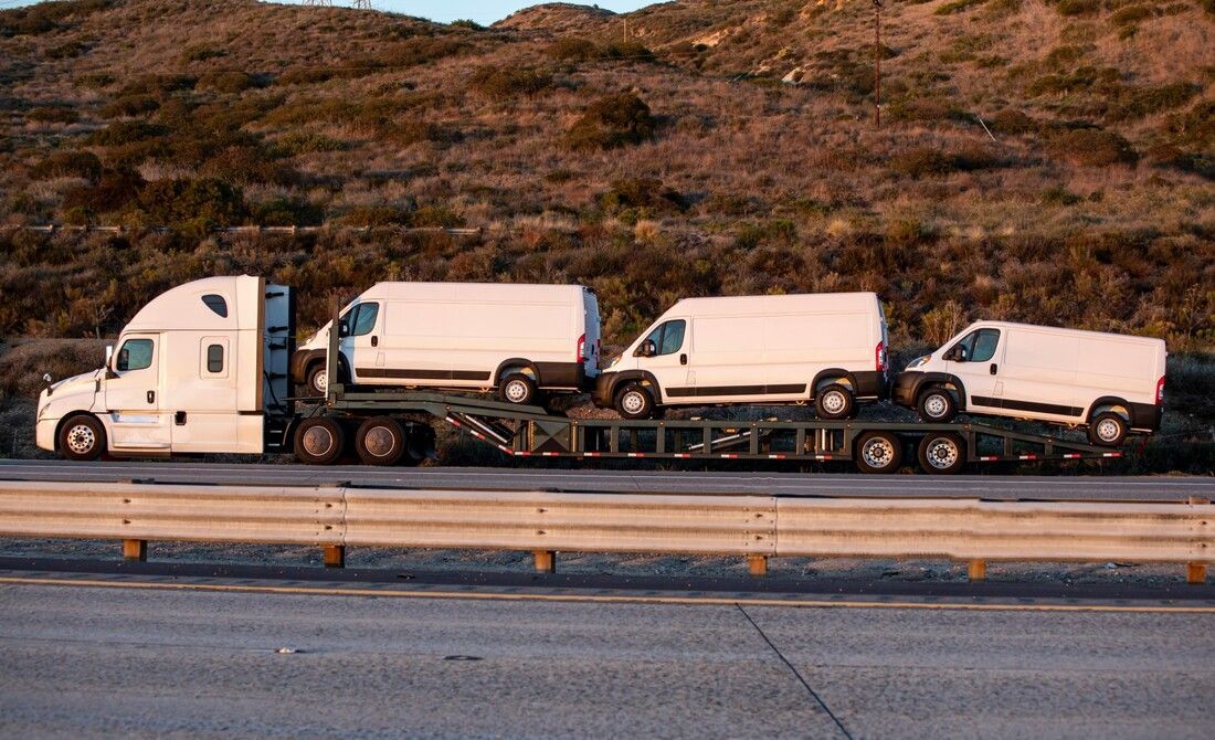 Large flatbed truck towing three white vans