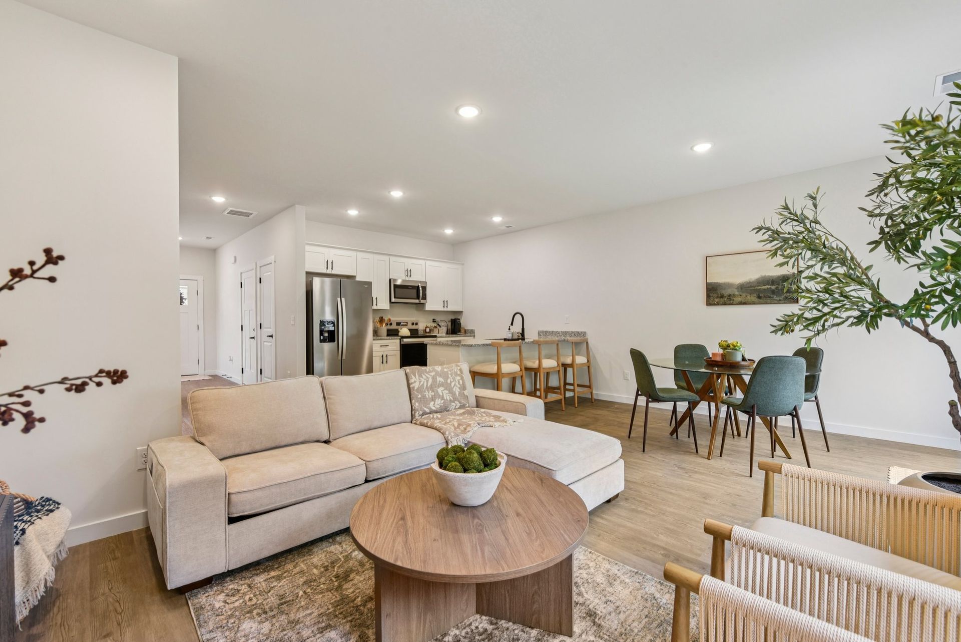 Open-concept living space with a kitchen, dining area, and seating. Light-toned decor with a sofa, chairs, and a round table.