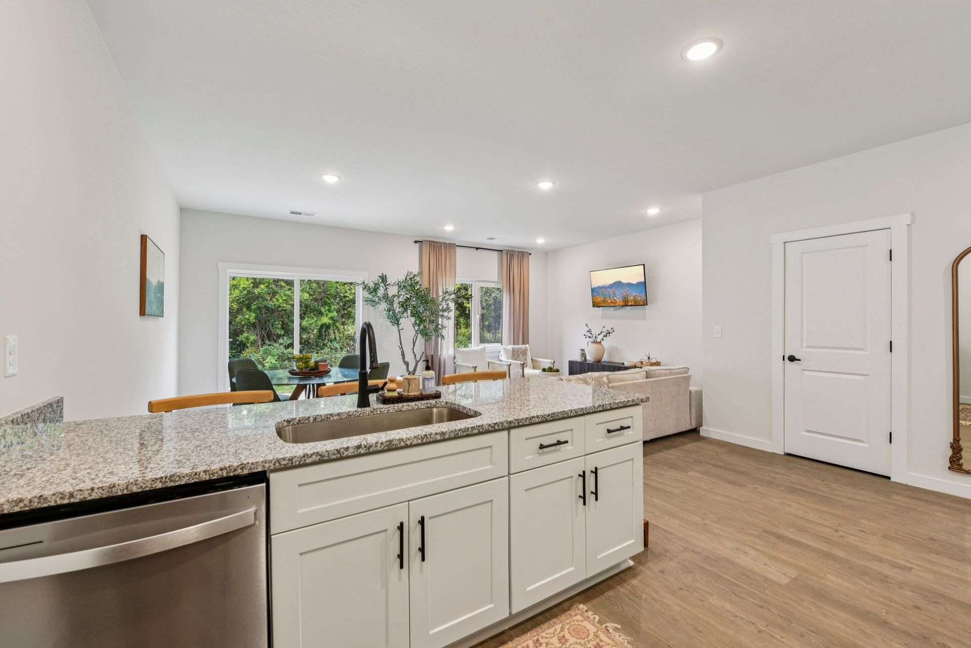 Kitchen island with granite countertop, sink, and white cabinets opens to a living area with large sliding doors.