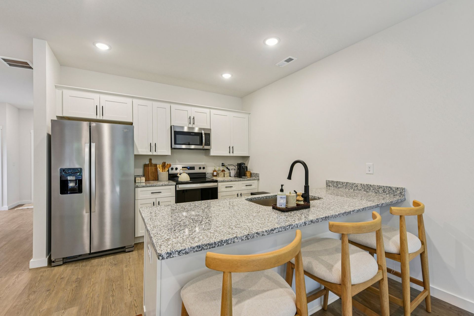 Modern kitchen with white cabinets, stainless steel appliances, granite countertops, and breakfast bar with stools.