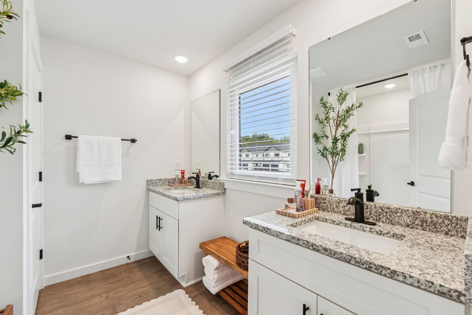 Bathroom with white cabinets, granite countertops, and two sinks. Light wood floor.