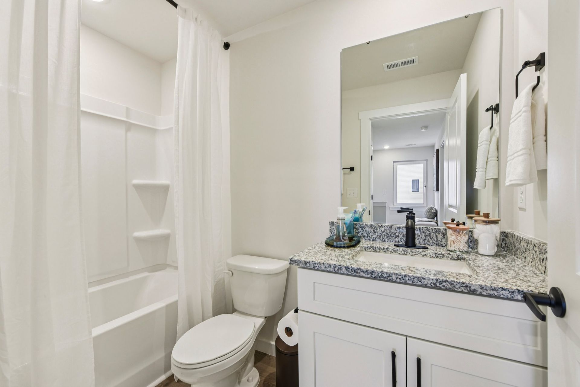 Bathroom with white walls, a tub/shower, toilet, and vanity with a granite countertop and large mirror.