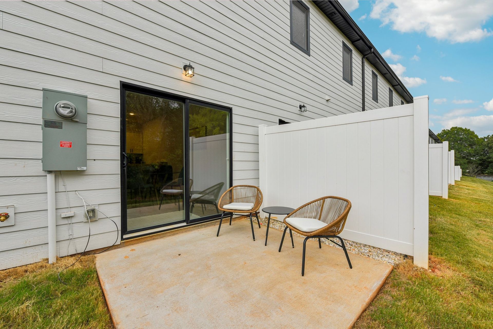 Patio with two chairs and small table next to a sliding glass door. White privacy fence on right.