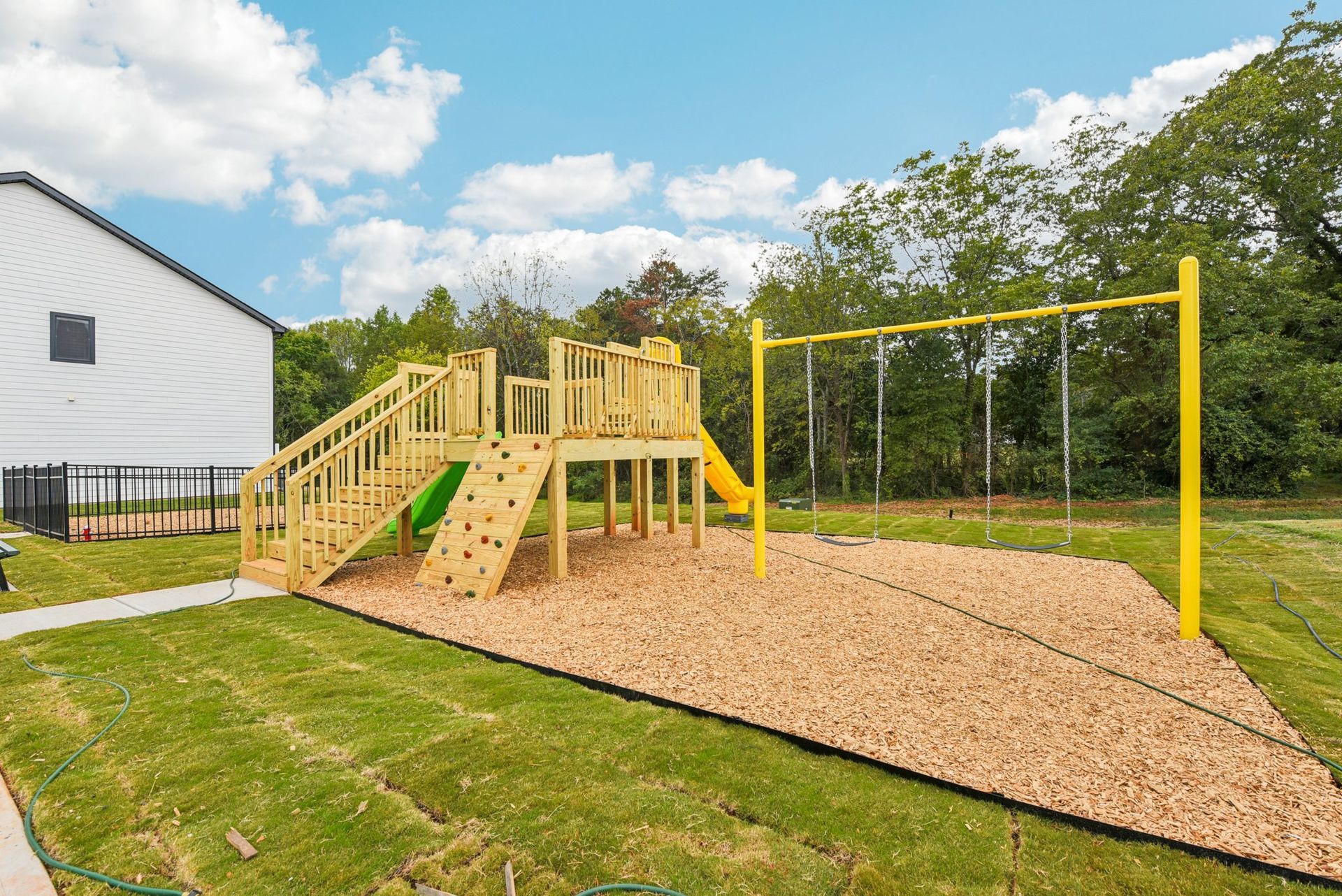 Playground with wooden structures, yellow swing set, and a slide on wood chips.