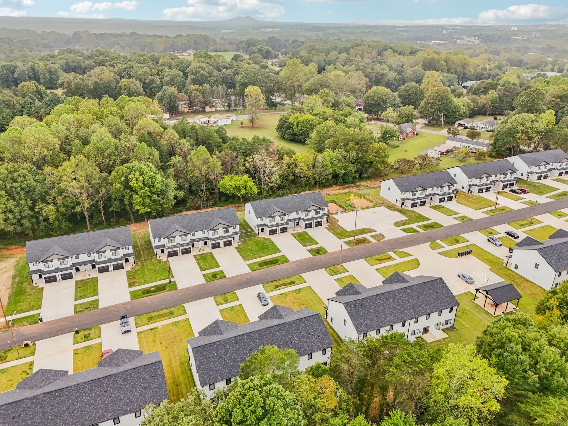 Aerial view of newly built townhouses with dark gray roofs, green lawns, and a road.