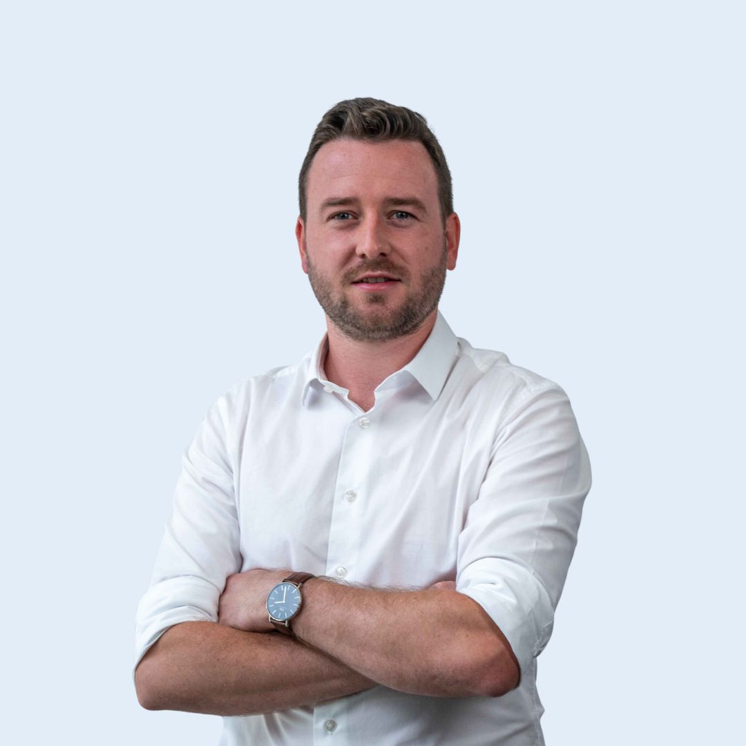A man wearing a white shirt and a watch is standing with his arms crossed.