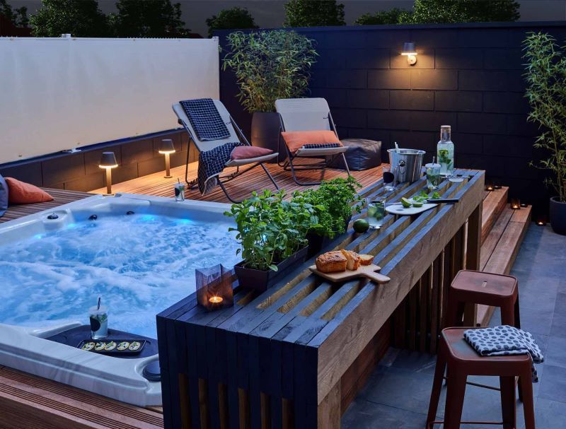 Nighttime patio with hot tub, bar, and lounge chairs; lit with soft lights.