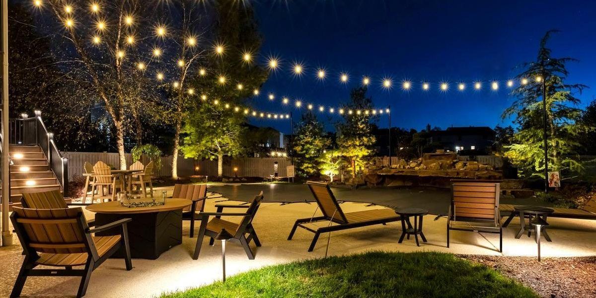 An outdoor patio at night with string lights, seating, and a fire pit.