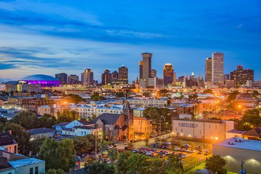 New Orleans skyline at dusk, buildings lit with golden lights, against a blue twilight sky.