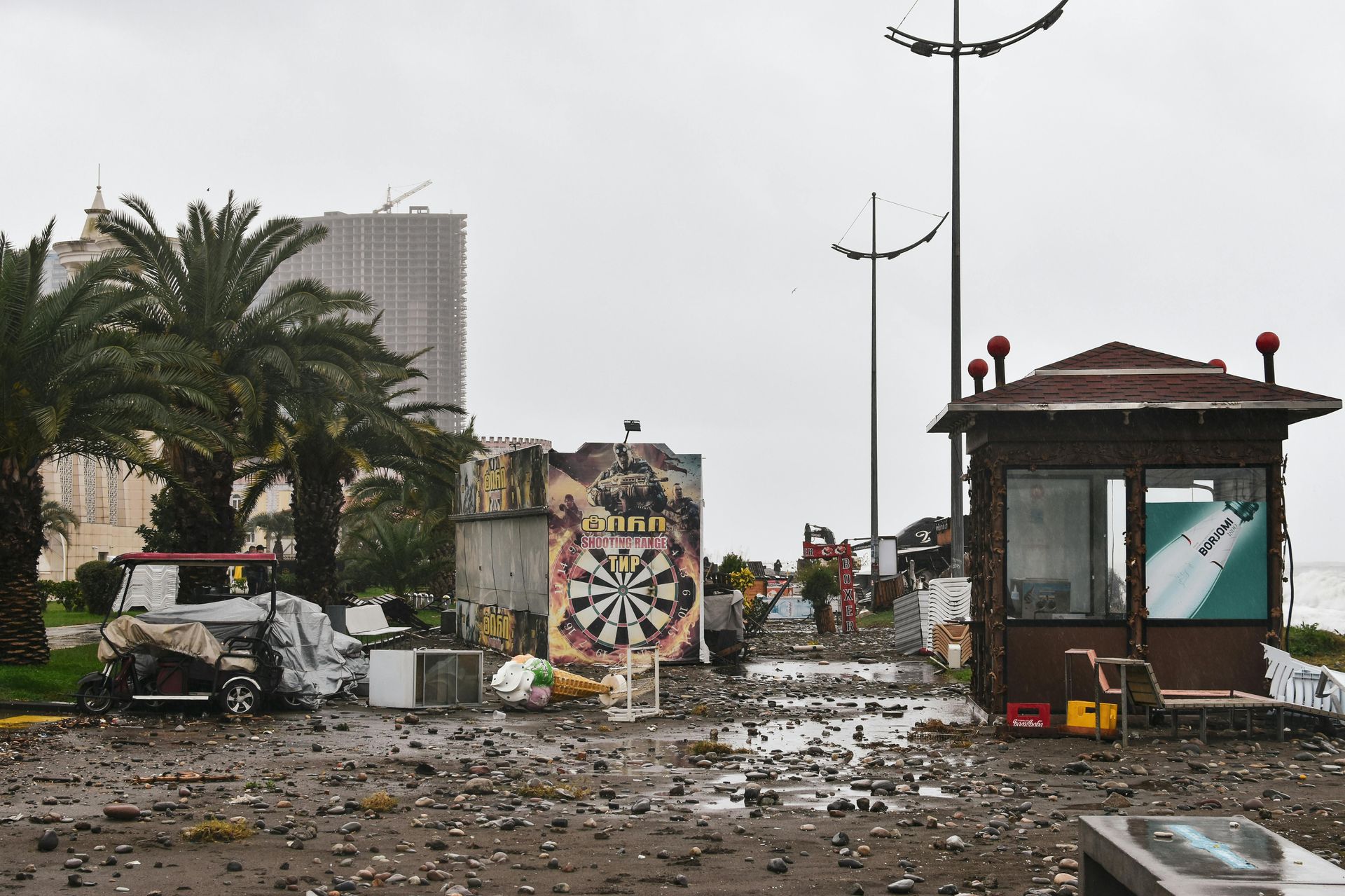 Coastal area with debris, a graffiti-covered structure with a dartboard, a small building.