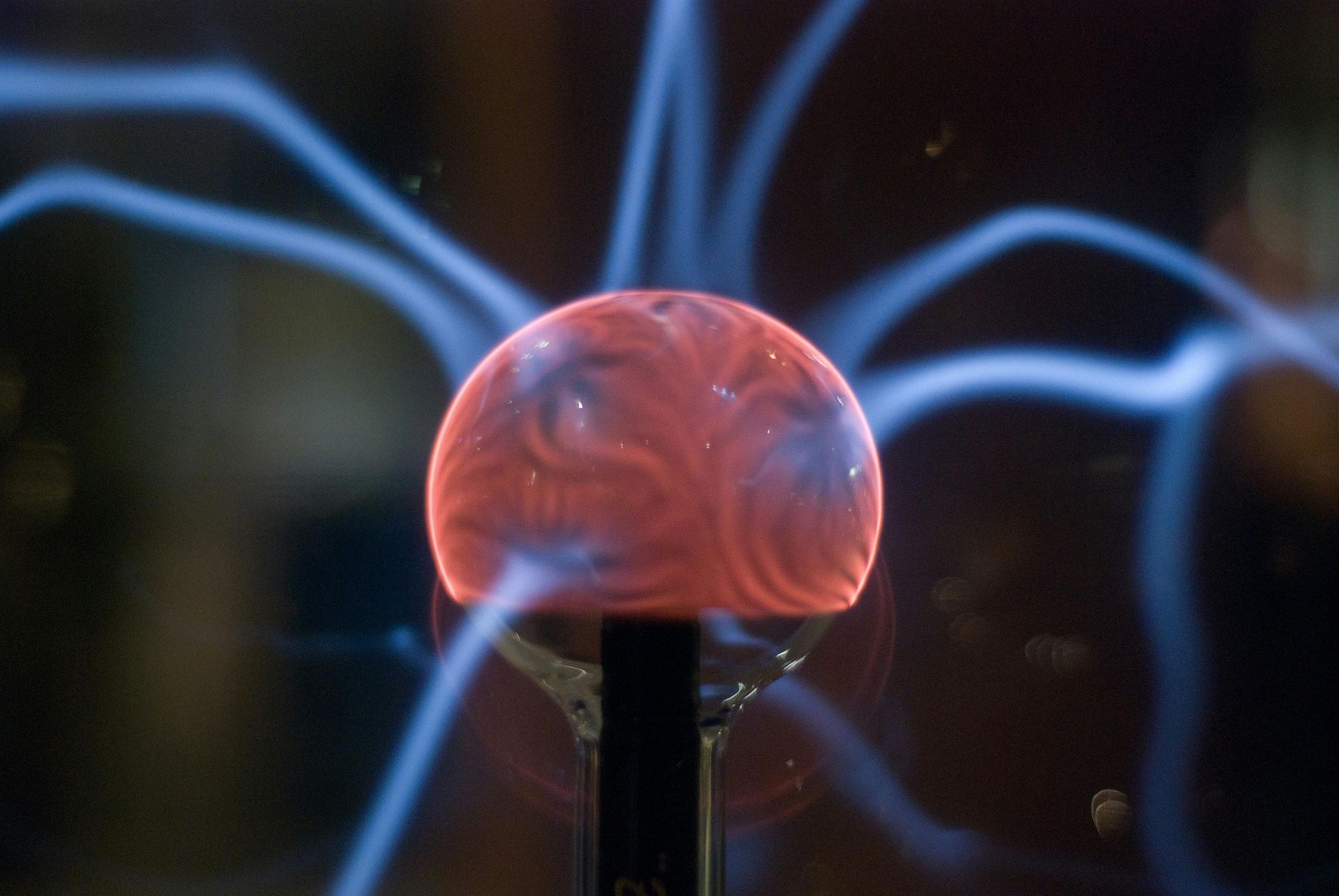 Glowing plasma ball with blue lightning-like arcs, red center, on a black stand.