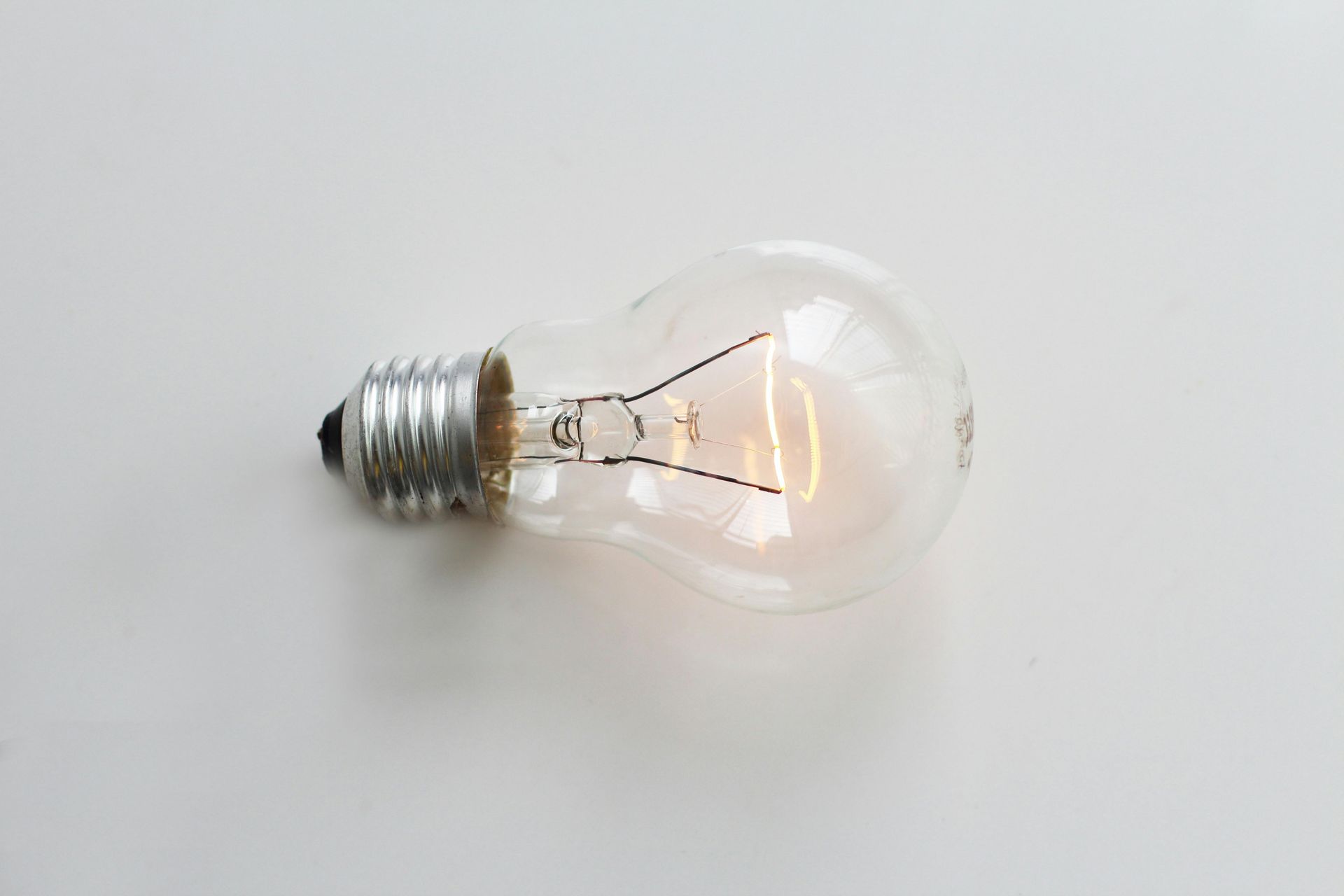 Light bulb, lit, on a white surface.