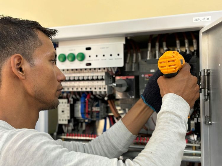 Man with a screwdriver working on electrical wiring inside a cabinet.