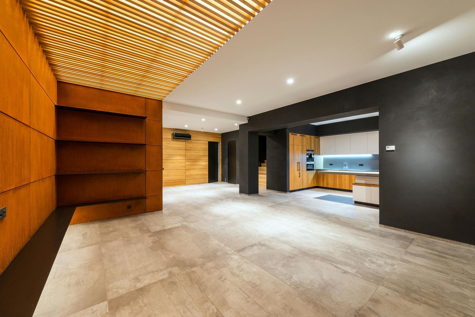 Modern interior with wood paneling, built-in shelves, and an open kitchen with black walls and tiled floor.