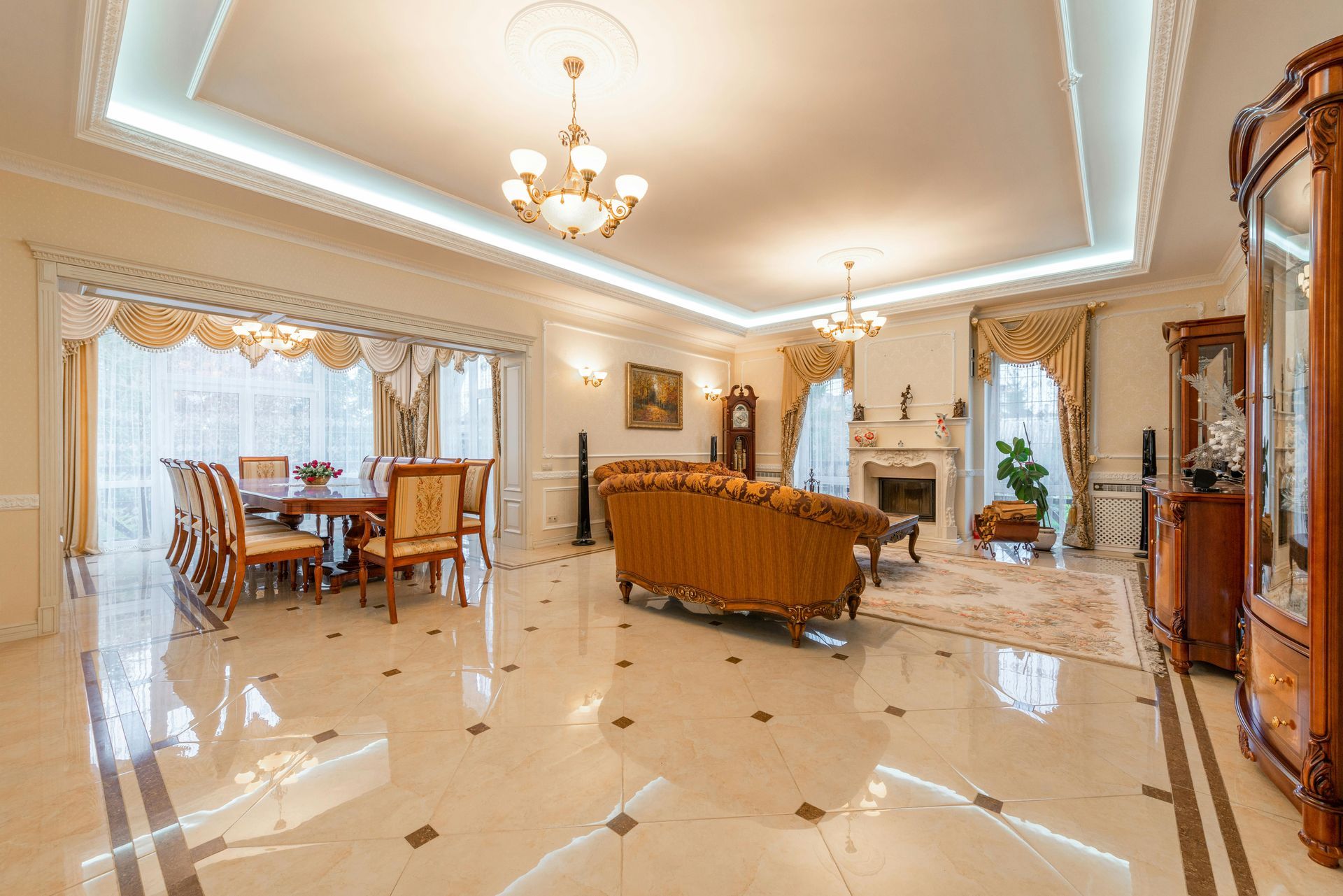 Elegant living room with dining area, fireplace, and ornate furniture. Beige, gold accents, shiny floor.