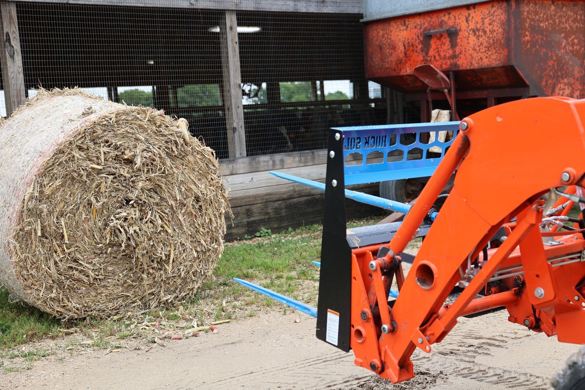 A large bale of hay is being loaded onto a tractor.