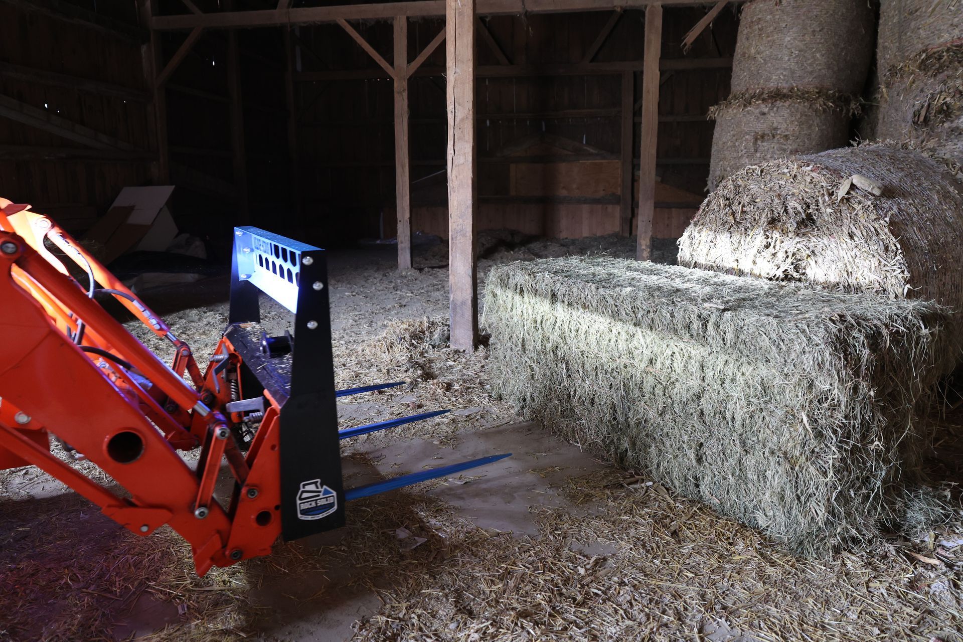 A tractor is loading hay bales in a barn