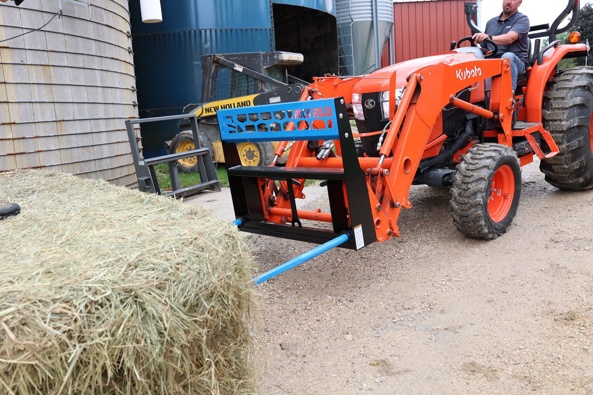 A man is driving a tractor with a hay bale attached to it.