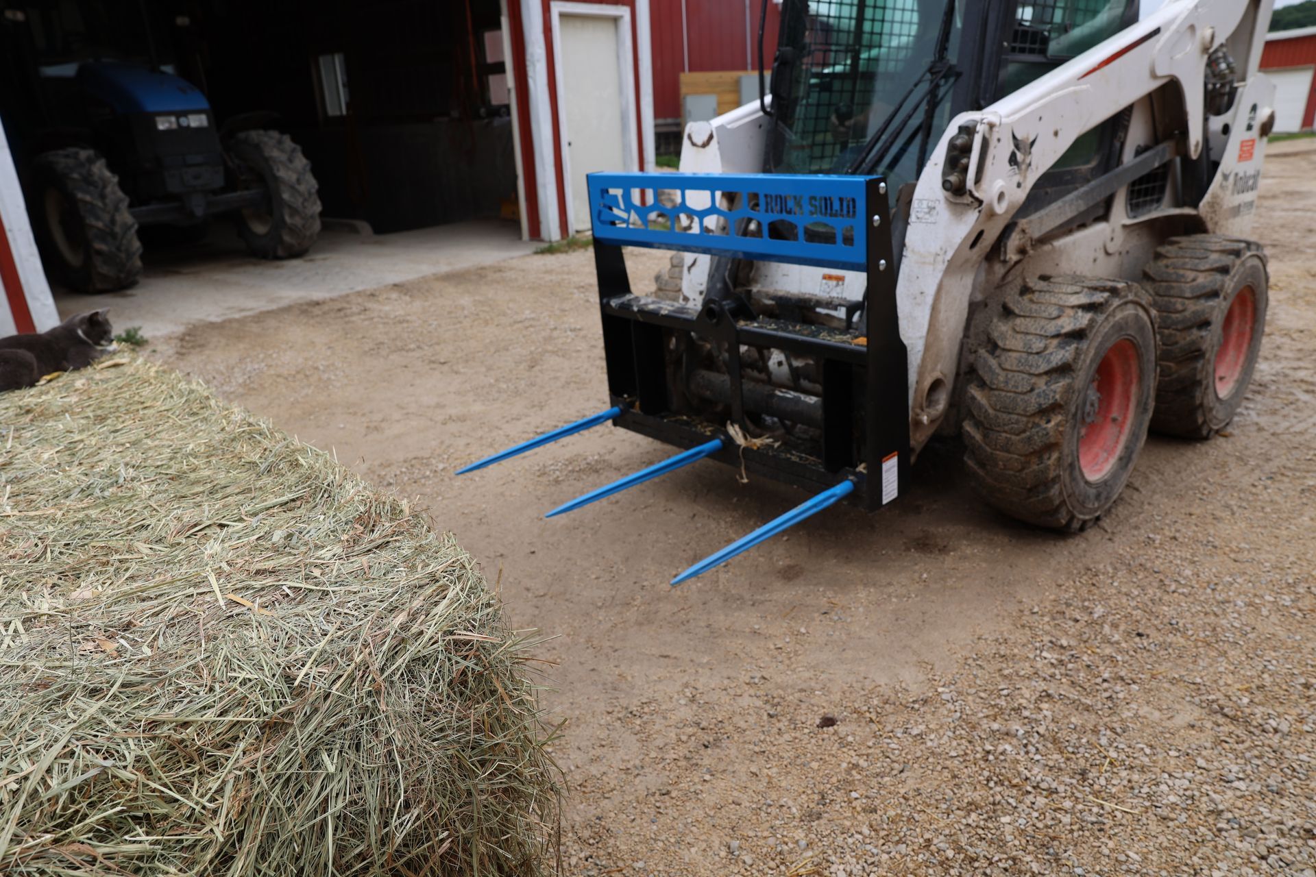 A bobcat with a bale of hay on the ground