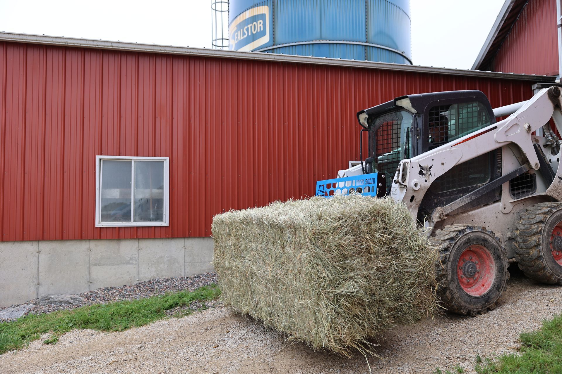 A bobcat is loading a bale of hay into a barn.