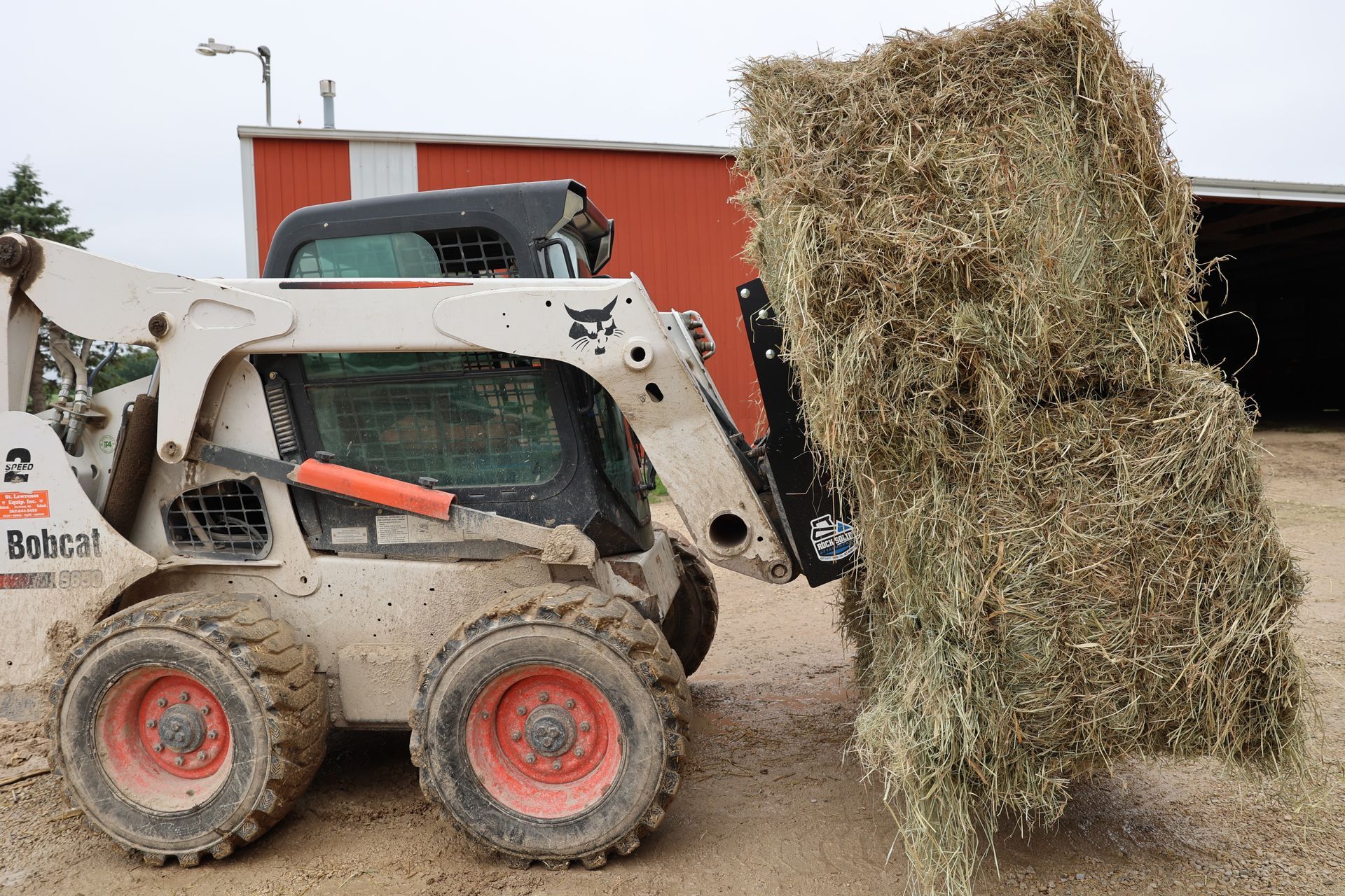 A bobcat is loading hay into a tractor.