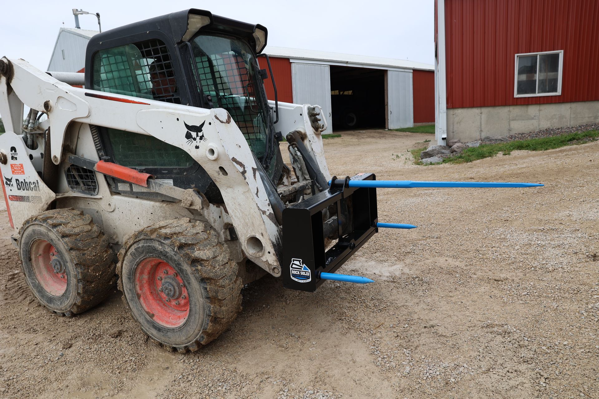 A bobcat is parked in a dirt lot in front of a red barn.