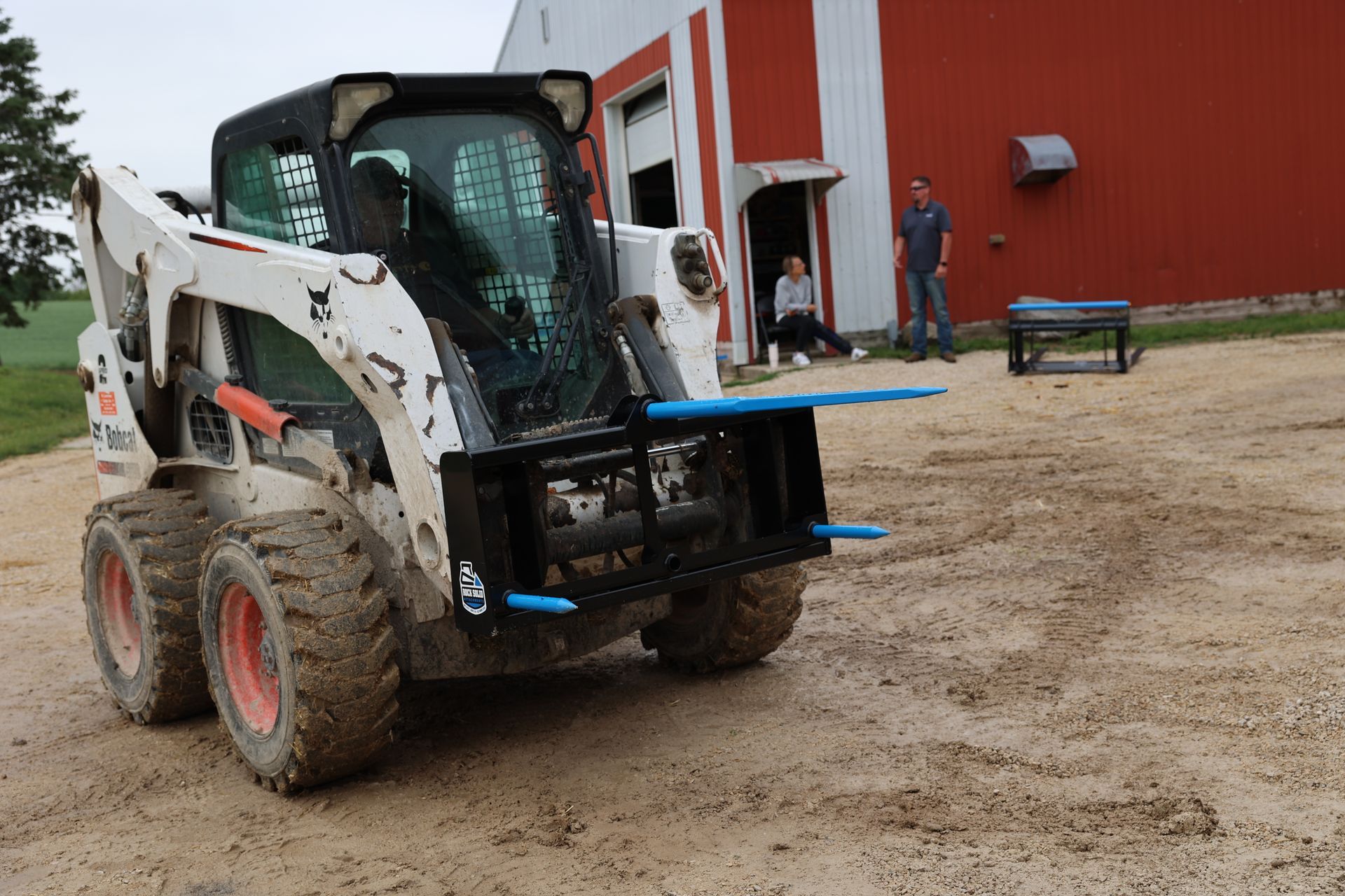 A bobcat is parked in a dirt lot in front of a red building.