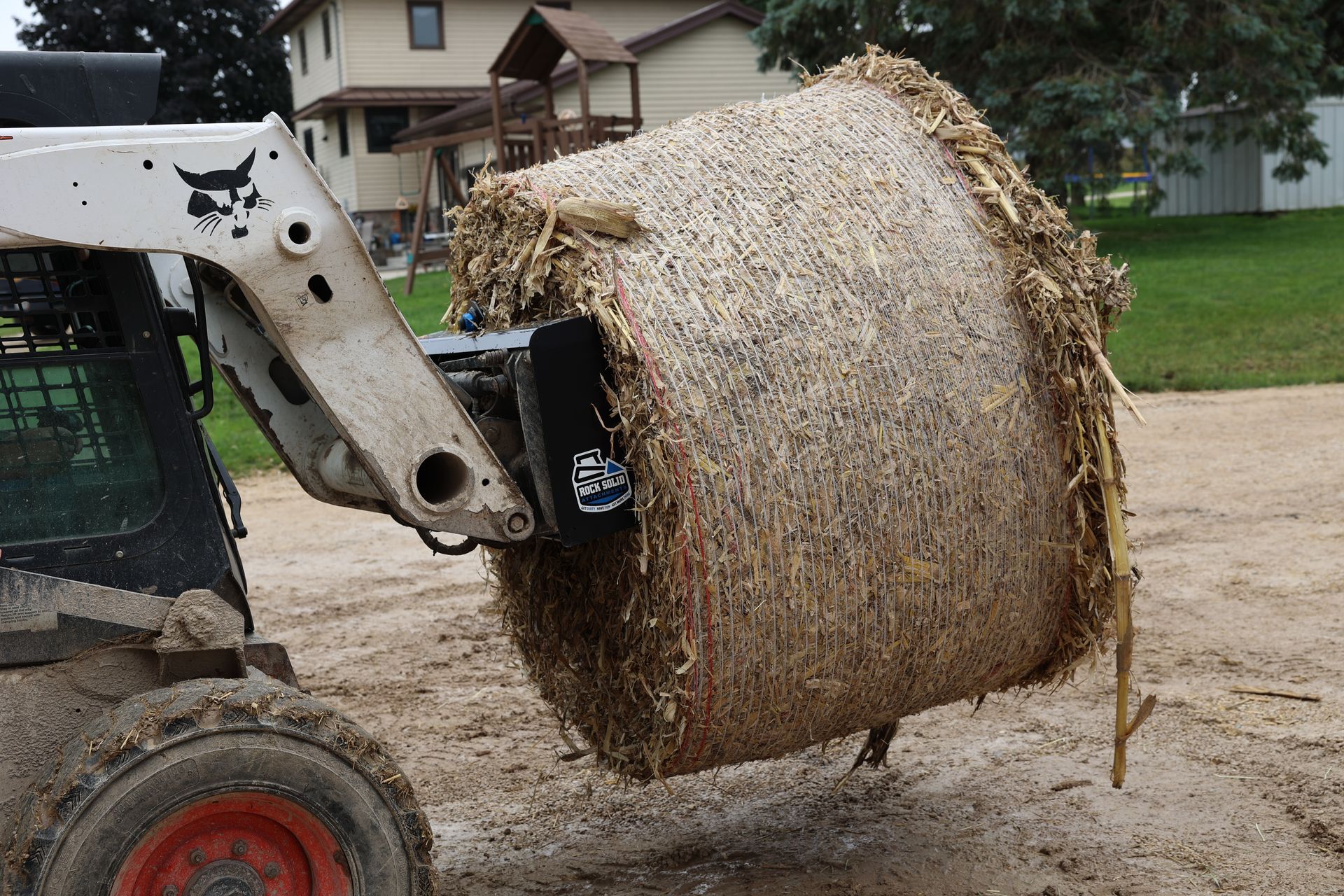 A large bale of hay is being lifted by a bobcat