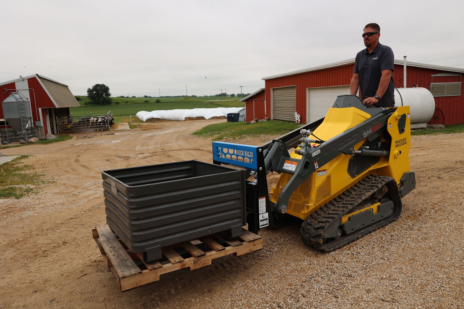 A man is driving a yellow tractor with a pallet attached to it.