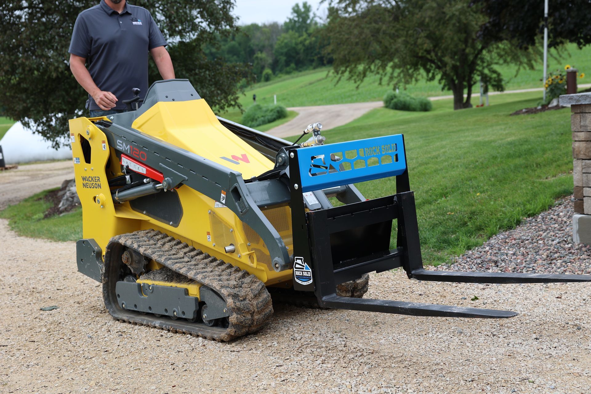 A man is standing next to a yellow tractor with forks attached to it.