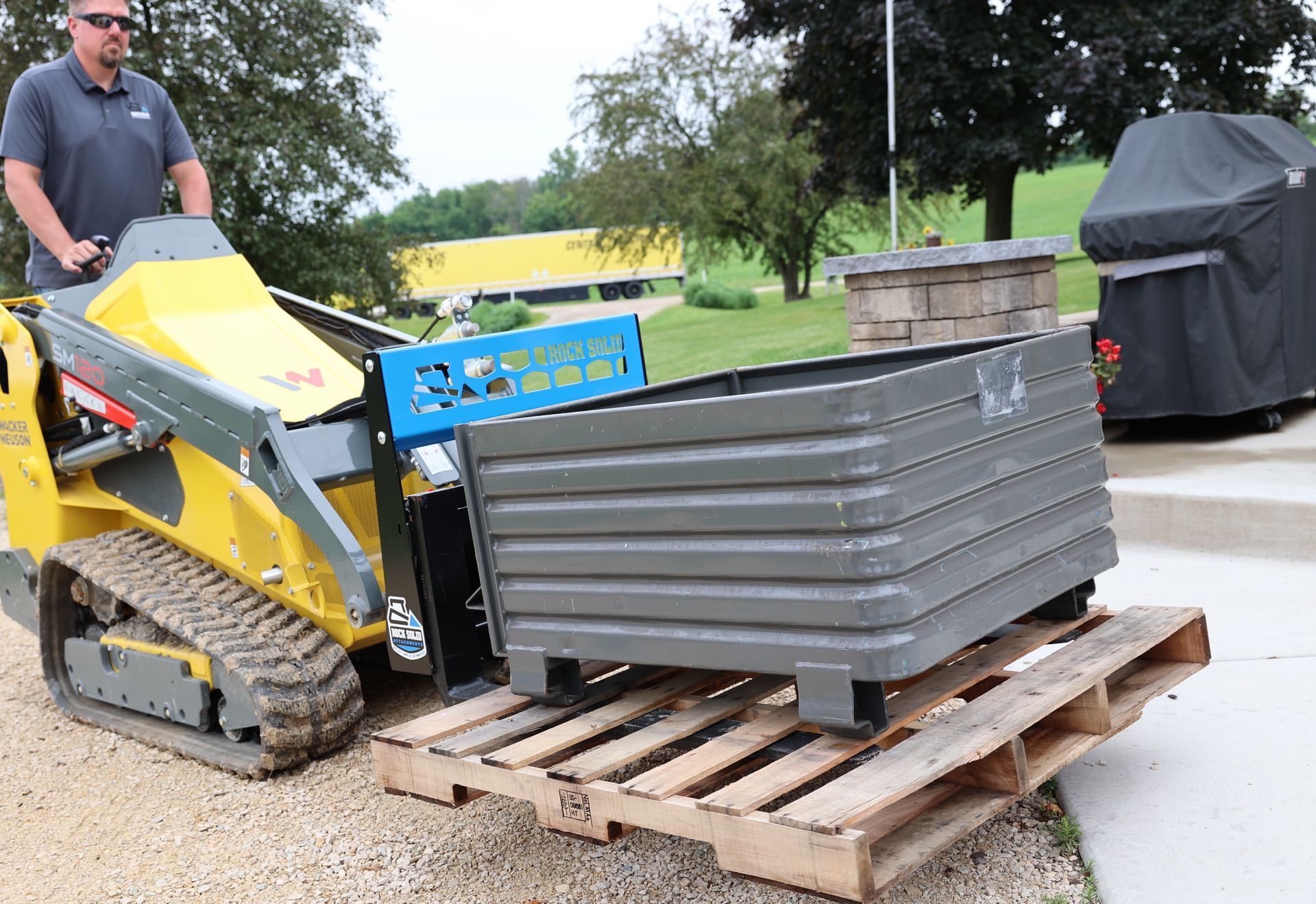 A man is driving a yellow and black tractor on a wooden pallet.