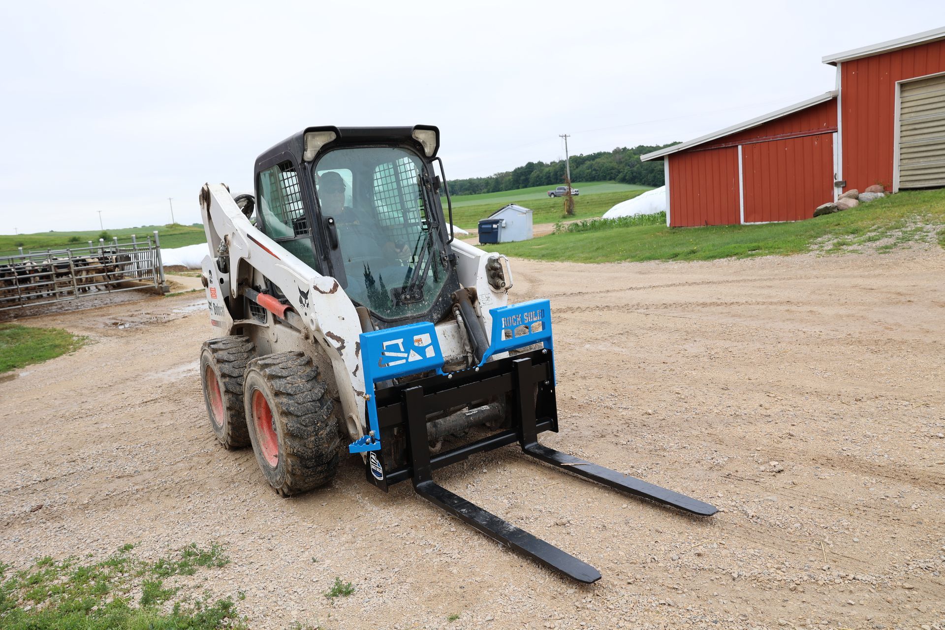 A bobcat with forks attached to it is driving down a dirt road.