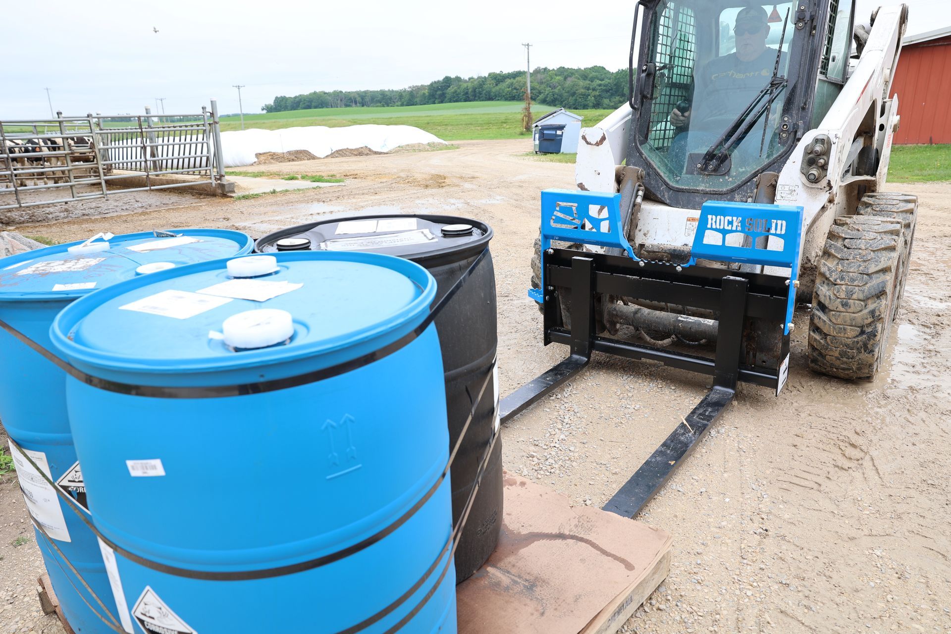 A bulldozer is loading barrels with chemicals on a pallet.