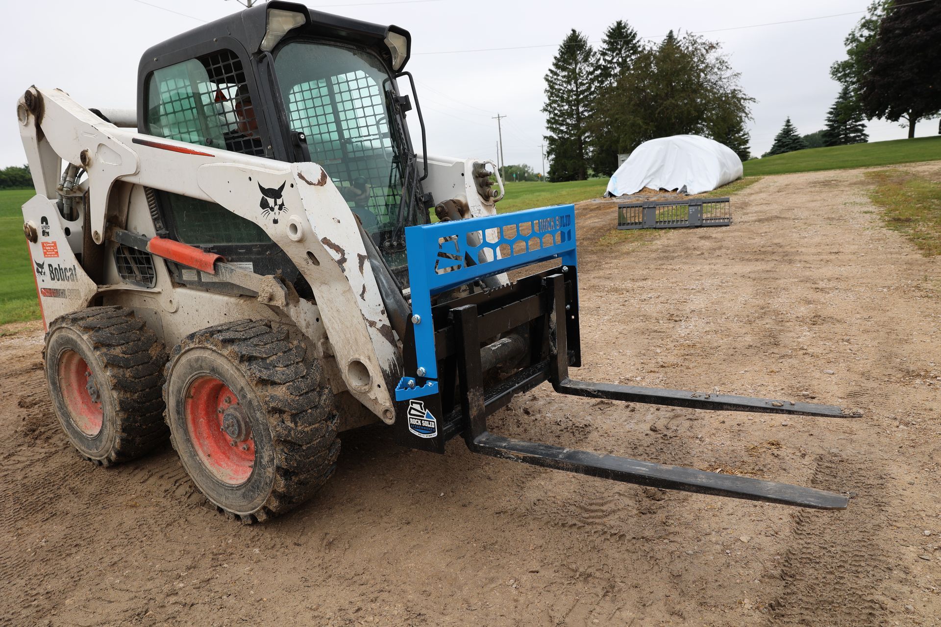 A bobcat with forks attached to it is parked on a dirt road.