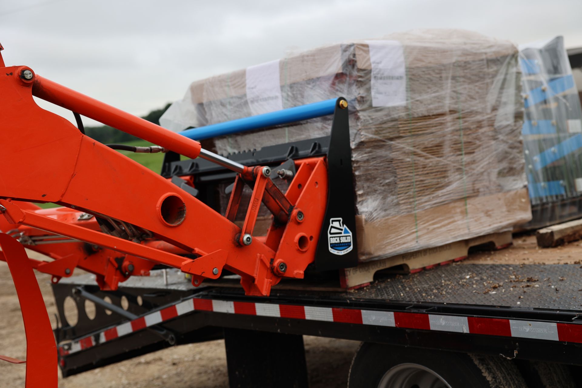 A tractor is loading a pallet of wood onto a flatbed trailer.