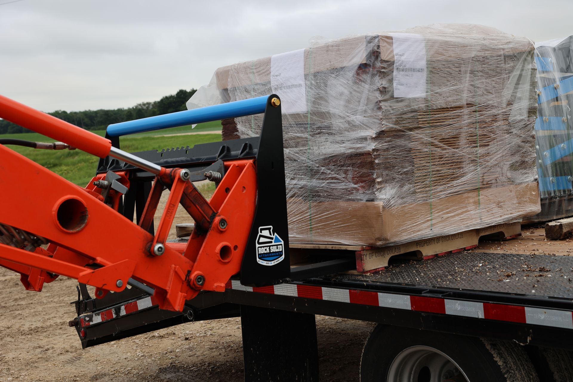 A forklift is carrying a large stack of bricks on a trailer.