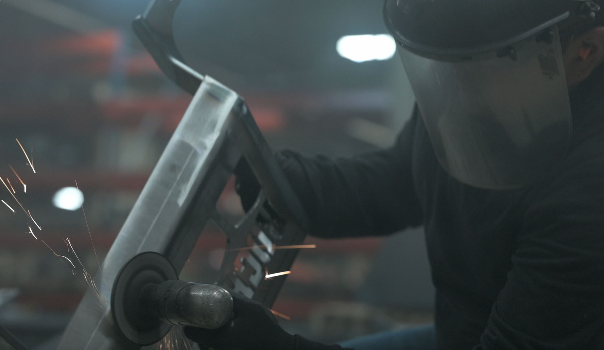 A man wearing a face shield is grinding a piece of metal.