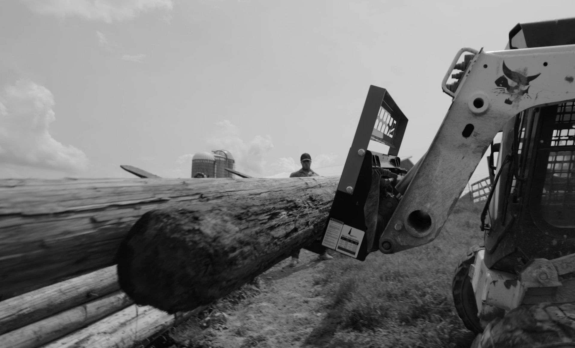 A black and white photo of a bulldozer carrying logs in a field.