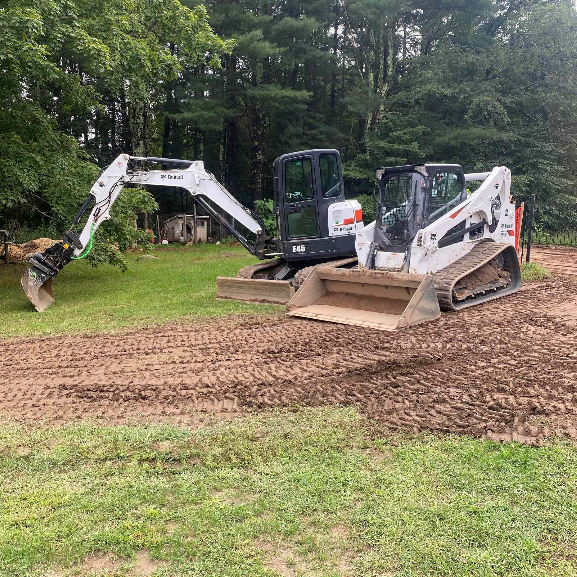Bobcat excavator and skid steer on muddy ground near trees.