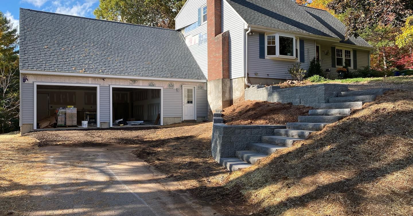 Gray house with attached garage, stairs on a hillside, and a driveway.