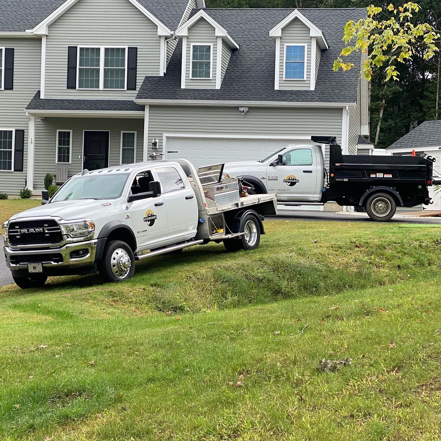 Two white work trucks parked in front of a house on a green lawn.