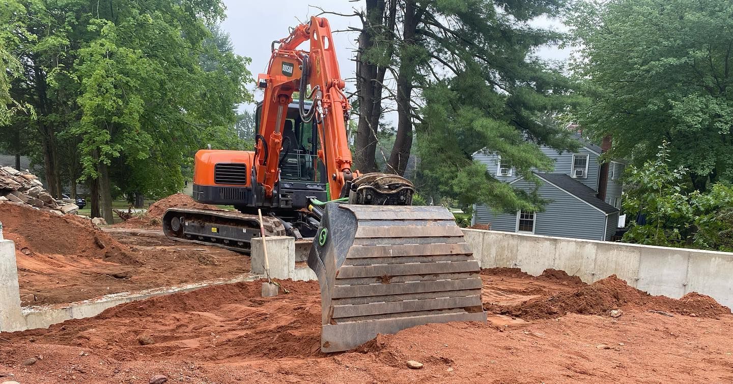 Orange excavator on a construction site, digging into red soil.